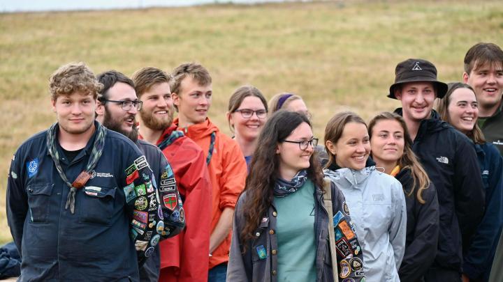 En gruppe af unge spejdere mellem 16 og 23 år, som er stillet op i forbindelse med en aktivitet på Spejdernes Lejr 2023. De smiler og ser glade ud.