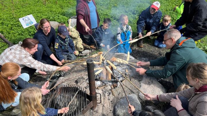 Familiespejdere og forældre, der laver snobrød omkring bålet